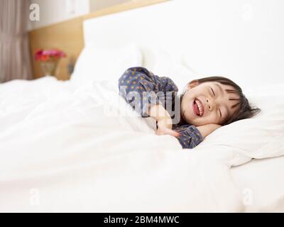 petite fille asiatique mignonne couché au lit en riant tout en se préparer à dormir Banque D'Images