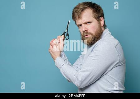 L'homme tient des ciseaux comme s'il s'agissait d'une arme, il n'avait pas visité un barbershop depuis longtemps et était prêt à couper ses cheveux par lui-même. Banque D'Images