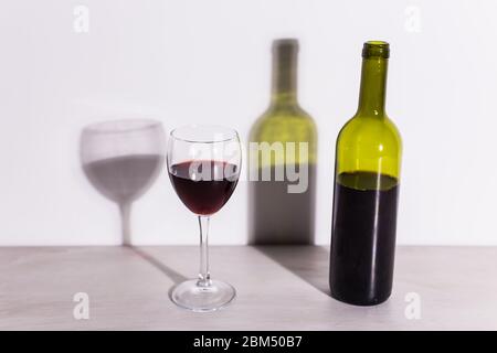 Un verre de vin et une bouteille jettent une longue ombre du soleil du soir. Banque D'Images
