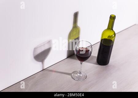 Un verre de vin et une bouteille jettent une longue ombre du soleil du soir. Banque D'Images