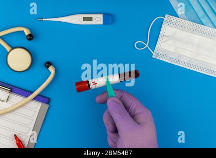 Composition à couche plate avec tube de test sanguin sur fond bleu. Masque médical antiviral pour la protection contre le coronavirus Banque D'Images