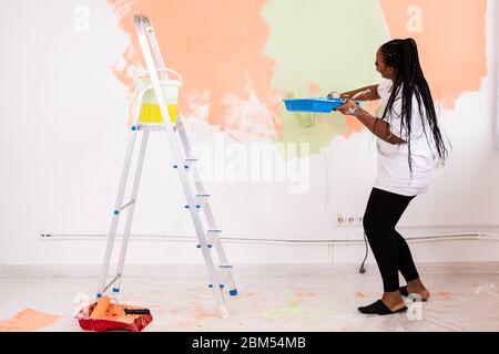 Jeune femme africaine américaine belle peinture mur dans son nouvel appartement. Concept de rénovation et de redécoration. Banque D'Images