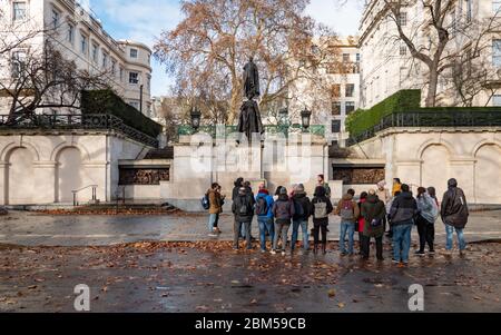 Un groupe de Londres sur le Mall étant présenté les monuments commémoratifs du roi George VI et de la reine Elizabeth lors d'une journée automnale humide à Londres Banque D'Images
