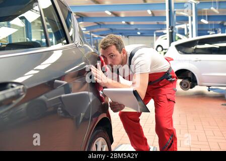 Le mécanicien de voiture examine le véhicule d'accident dans un atelier après la peinture Banque D'Images