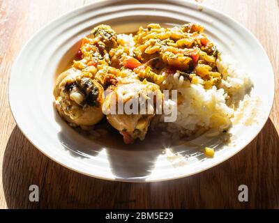 Portion de Chakhokhbili (plat traditionnel géorgien à base de poulet ragoût, de tomate, d'aubergine et d'herbes fraîches) avec du riz cuit sur une assiette blanche sur une plaque en bois Banque D'Images