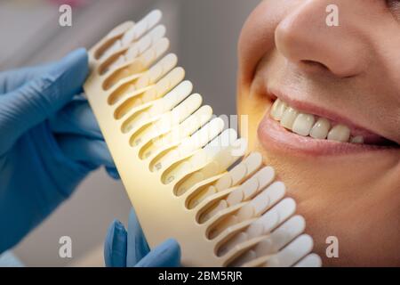vue rognée du dentiste dans des gants en latex tenant la palette de dents près de l'homme souriant Banque D'Images