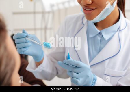 vue rognée du dentiste afro-américain dans des gants en latex tenant la brosse à dents et la brosse de nettoyage interdentaire près du patient Banque D'Images