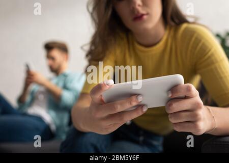 Foyer sélectif de fille avec smartphone assis près de petit ami sur le canapé Banque D'Images