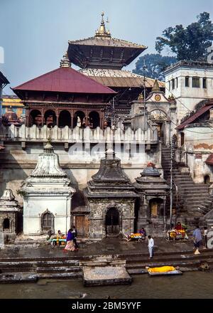 Katmandou, Népal - novembre 1986: Les coursiers se préparent à une cérémonie de crémation aux Ghats par le temple de Pashupatinath, Katmandou, sur les rives de la rivière Bagmati. Film 35 mm numérisé. Banque D'Images