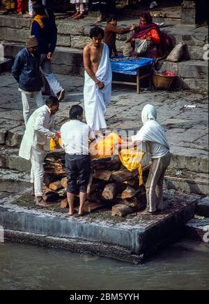 Katmandou, Népal - novembre 1986: Les coursiers se préparent à une cérémonie de crémation aux Ghats par le temple de Pashupatinath, Katmandou, sur les rives de la rivière Bagmati. Film 35 mm numérisé. Banque D'Images