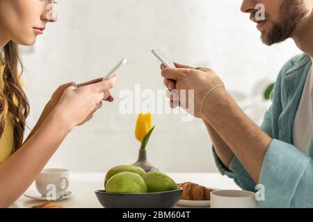 Vue réduite d'un couple discutant avec un smartphone pendant le petit déjeuner dans la cuisine Banque D'Images