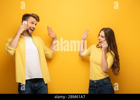 Couple joyeux se faisant passer les mains les uns sur les autres tout en parlant sur un fond jaune sur un smartphone Banque D'Images