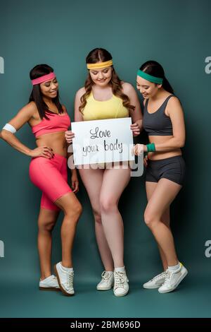 Les sportifs multiethniques sourient et montrent l'étiquette avec amour votre corps lettrage sur fond vert Banque D'Images