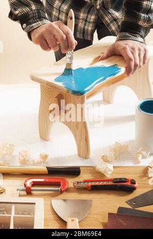 Vernissage à la main en bois Artisan un tabouret à la maison avec un revêtement bleu sur une table de travail, les mains close up Banque D'Images