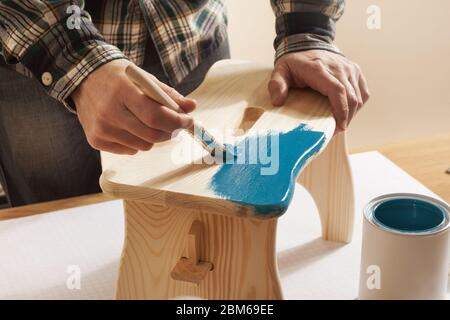 Vernissage à la main en bois Artisan un tabouret à la maison avec un revêtement bleu sur une table de travail, les mains close up Banque D'Images