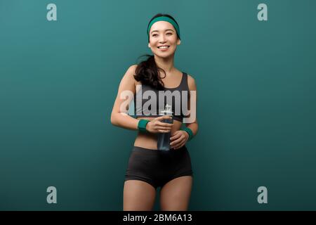 Vue de face de l'asian sportswoman avec bouteille de sport souriante isolée sur le vert Banque D'Images