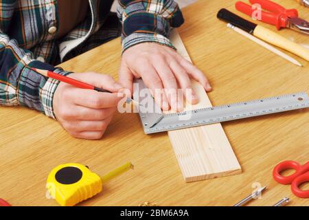 L'homme travaillant sur un projet de bricolage et la mesure d'une planche en bois avec des outils de travail tout autour, les mains close up Banque D'Images