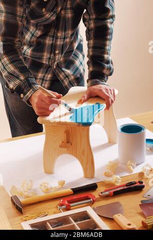 Artisan vernis un tabouret en bois fait à la main à la maison avec un revêtement bleu sur une table de travail Banque D'Images