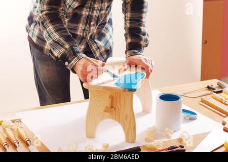 Artisan vernis un tabouret en bois fait à la main à la maison avec un revêtement bleu sur une table de travail Banque D'Images