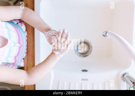 Une jeune fille blonde se lavant les mains avec un savon dans la cuisine avant de manger. Concept d'hygiène et de santé Banque D'Images