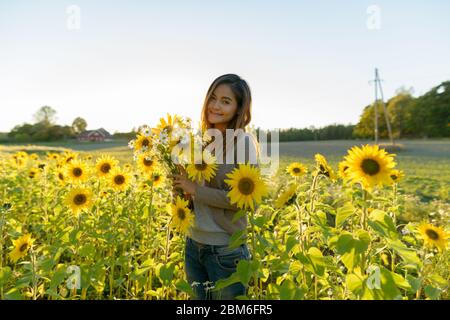 Jeune femme asiatique belle tenant des fleurs dans la ferme de jardin de tournesol Banque D'Images