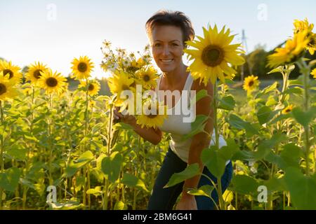 Bonne mature belle femme tenant des fleurs dans la ferme de jardin de tournesol Banque D'Images