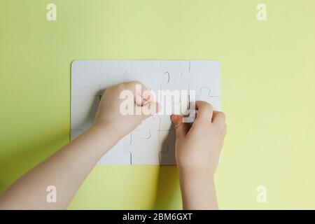 Main d'enfant mettre la dernière pièce de puzzle blanc sur fond jaune Banque D'Images