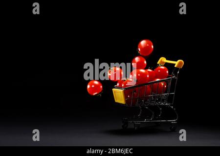 Mini panier avec tomates cerises fraîches sur fond noir. Espace de copie de publicité de supermarché. Épicerie. Livraison de tomates. Transport Banque D'Images