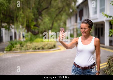 Bonne mature belle femme touristique prenant selfie dans les rues de la ville à l'extérieur Banque D'Images