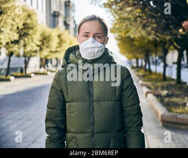 Portrait d'une femme dans un masque, à l'extérieur dans une rue vide, arbres verts en plein soleil sur un fond. Distanciation sociale pendant la quarantaine mondiale du coronavirus Banque D'Images