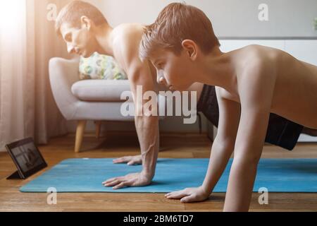 Garçon avec son père faisant du yoga à la maison en quarantaine. Père et fils en posture de planche Banque D'Images