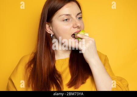 Belle fille mangeant la pomme verte, debout sur un fond de mur jaune. Régime alimentaire et concept de nutrition approprié. Photo pour l'article, la bannière ou la circulaire Banque D'Images