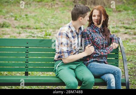 Jeunes couples flirtant en chemises à carreaux assis sur un banc dans le parc Banque D'Images
