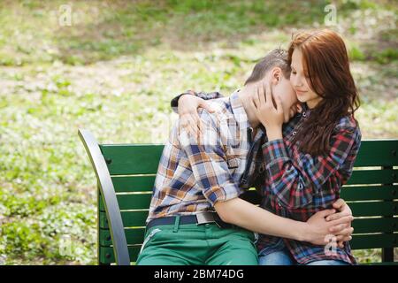 Jeunes couples en chemises à carreaux, assis sur un banc dans le parc, qui flirtent et embrasent Banque D'Images