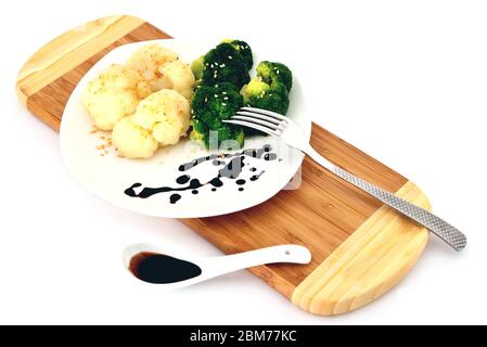 brocoli et chou-fleur sur une assiette sur un plan de coupe, fourchette et sauce dans une cuillère, fond blanc gros plan Banque D'Images