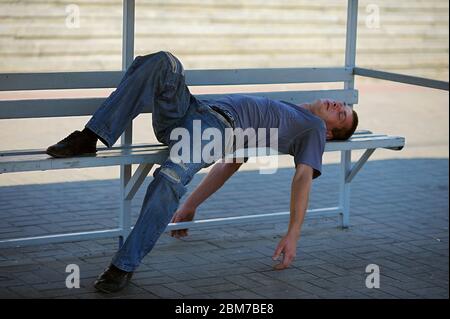 Homme s'endormant sur le banc de l'arrêt de bus dans la chaleur étouffante. 5 juillet 2012. Kiev, Ukraine Banque D'Images