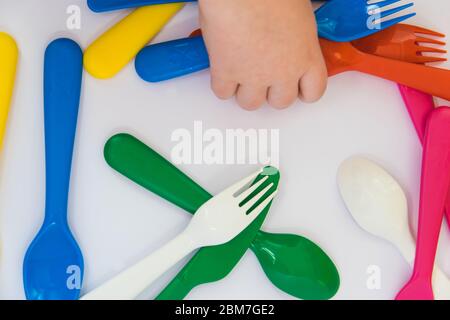 Fourchette en plastique bleu à la main du petit enfant. Vaisselle colorée sur fond blanc. Banque D'Images