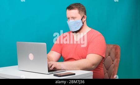Portrait d'un homme de brunette gai avec masque médical chirurgical travaillant sur la saisie d'un ordinateur portable de messagerie ou de discuter en social. Banque D'Images