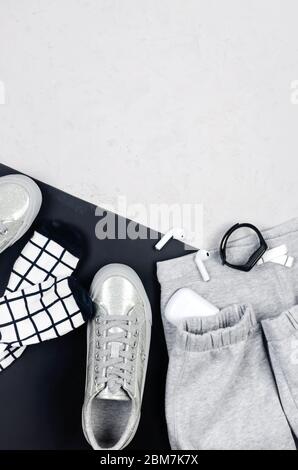 Arrière-plan monochrome pour femmes. Vêtements de sport gris, bracelet et écouteurs de fitness, baskets, chaussettes et pantalons tricotés sur fond gris et noir. Banque D'Images