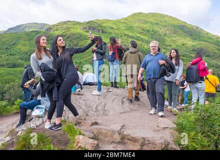 Deux jeunes touristes féminins prenant un selfie d'eux-mêmes avec une montagne en arrière-plan à Glenfinnan dans les Highlands d'Écosse, Royaume-Uni Banque D'Images