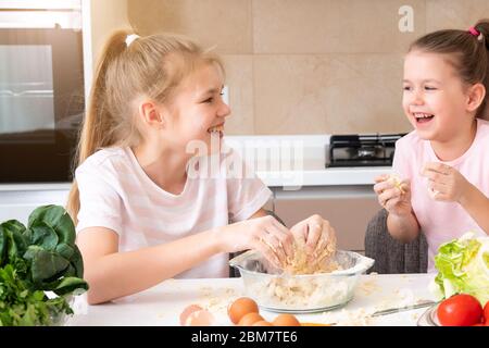 famille heureuse les enfants drôles préparent la pâte, cuisent des biscuits dans la cuisine. les sœurs s'amusent ensemble en riant Banque D'Images