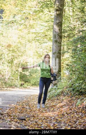 Jeune femme hitchhiker debout sur le côté de la route en forêt d'automne, à pied pour la ramasser. Banque D'Images