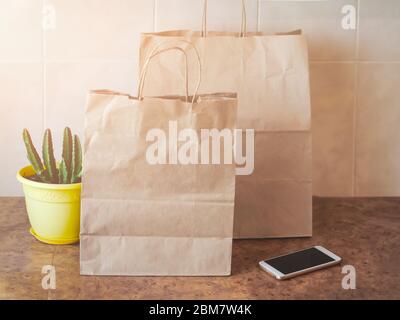 Sacs en papier, téléphone portable et une maison dans une casserole jaune sur une table de cuisine. Achat en ligne et livraison sans contact. Banque D'Images