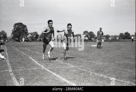 Sports d'école secondaire, Angleterre, c1960, à l'extérieur sur une piste de gazon, deux jeunes hommes en compétition dans une course de sprint sont cou et cou comme ils font un dernier deuxième tiret pour la bande de finition et pour gagner la course. Banque D'Images