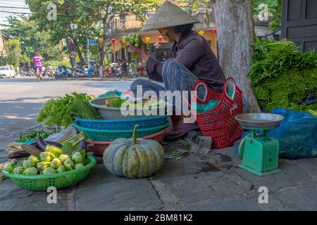 Hoi an, Vietnam - 12 avril 2018 : une femme qui vend des légumes dans la rue et qui regarde loin de l'appareil photo Banque D'Images