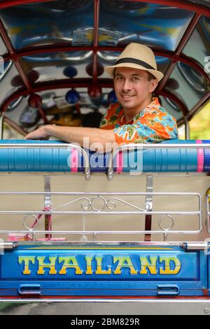 Joyeux jeune homme de tourisme charmant à cheval sur le tuk tuk dans la ville de Bangkok Banque D'Images