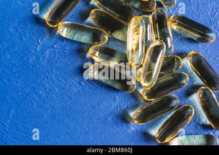Les capsules de gélatine transparente à l'huile de poisson reposent sur une surface bleue texturée. Acides gras polyinsaturés essentiels oméga-3 Banque D'Images
