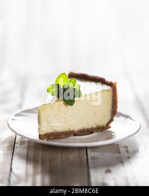 Tranche de cheesecake New York classique avec une branche de menthe sur une plaque sur une table en bois. Le concept de la boulangerie et des desserts aux gâteaux sucrés Banque D'Images