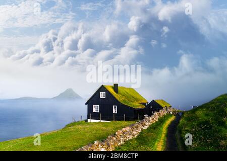 Matin brumeux vue d'une maison typique avec toit d'herbe à gazon haut et bleu ciel nuageux dans le village de Velbastadur sur Streymoy island, îles Féroé, Danemark. Photographie de paysage Banque D'Images