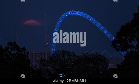 Wembley, Royaume-Uni. 7 mai 2020. La lune de fleurs (signifiant les fleurs de May en fleur), s'élève derrière l'arche du stade Wembley (éclairé en bleu pour les travailleurs du NHS) dans le nord-ouest de Londres. C'est la dernière superlune de 2020, où la lune est la plus proche de la terre (le périgée) et semble 6% plus grande qu'une pleine lune normale. Le stade Wembley est considéré comme un lieu neutre pour accueillir les matchs de la Premier League dans le cadre du projet Restart afin que la saison de football se termine après avoir été suspendue en raison de la pandémie du coronavirus. Credit: Stephen Chung / Alay Live News Banque D'Images